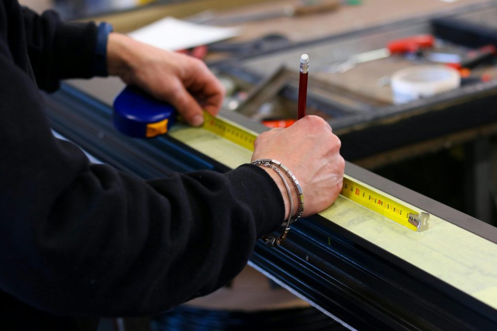 Un ouvrier mesurant l'aluminium avec un ruban à mesurer dans un atelier, démontrant sa précision et son savoir-faire.