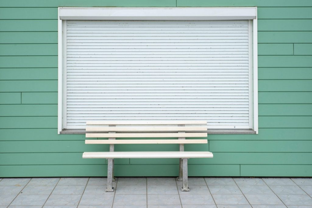Banc en bois simple, adossé à un mur végétal avec volet roulant fermé. Idéal pour une décoration minimaliste.